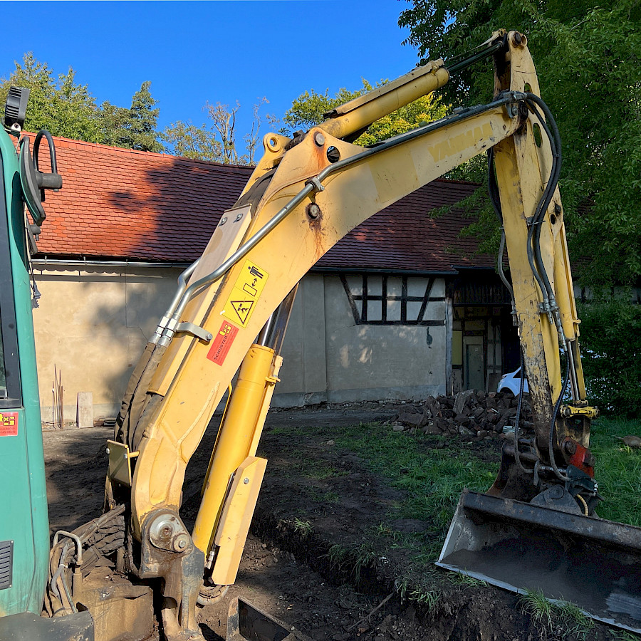 Gelber Bagger auf der Wiese vor dem Scheunenhaus