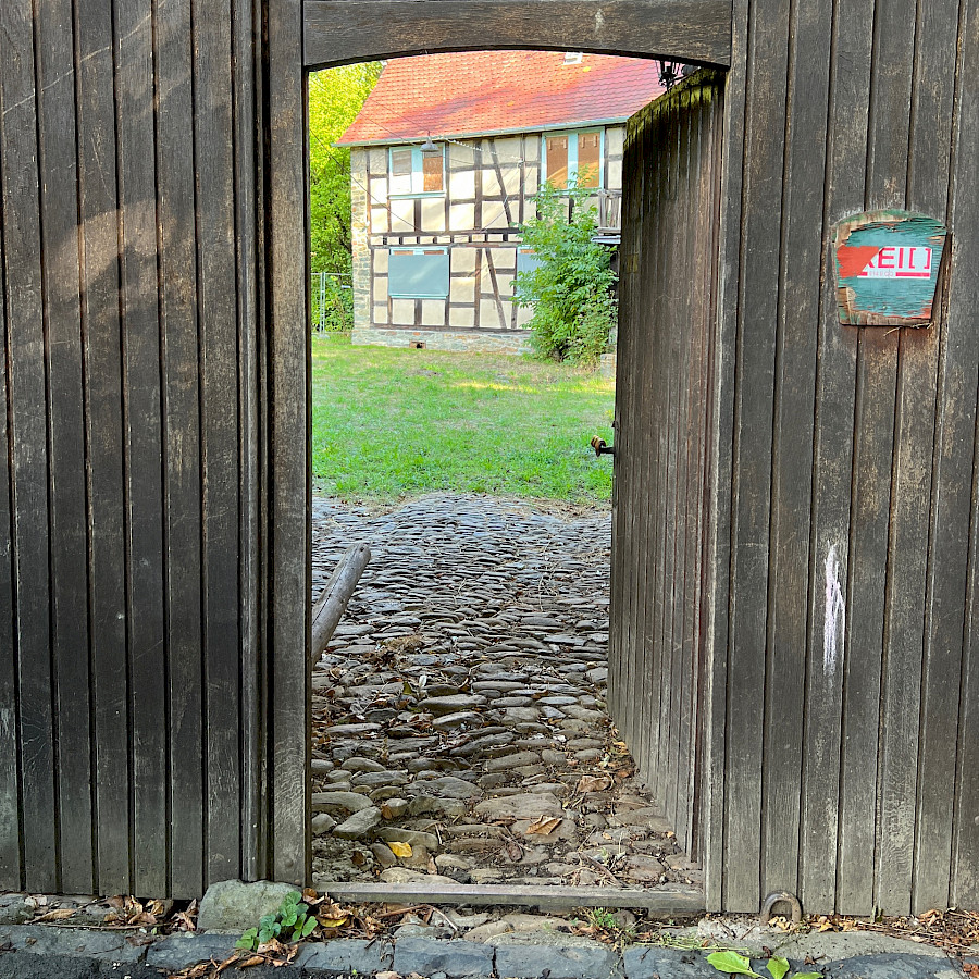 Blick auf das Haupthaus durch das geöffnete Holztor des Torgebäudes