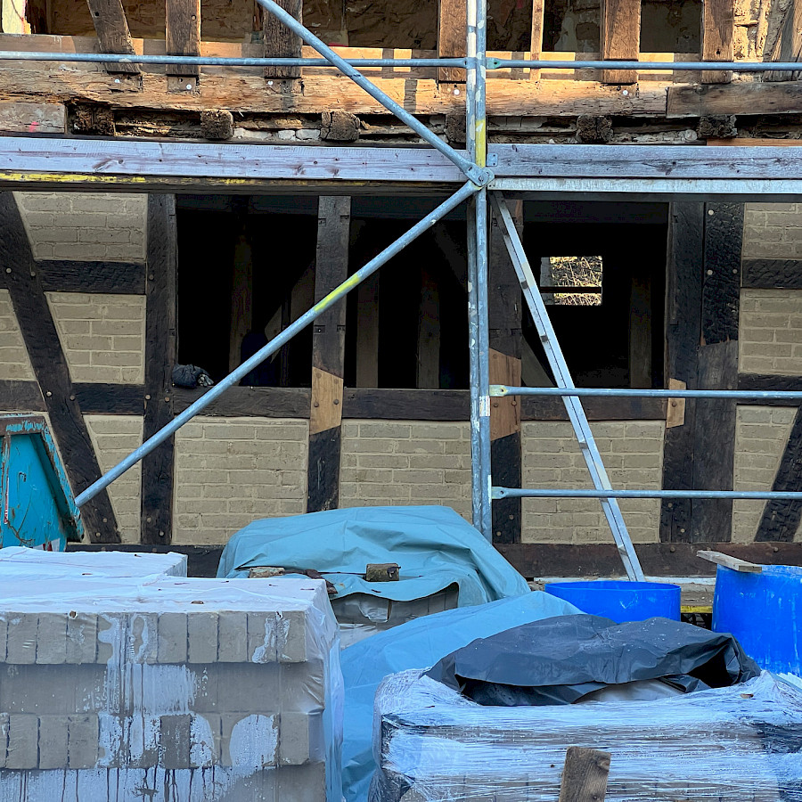 Ausschnitt Haupthaus mit Baugerüst, davor Lehmziegel und anderes Baumaterial