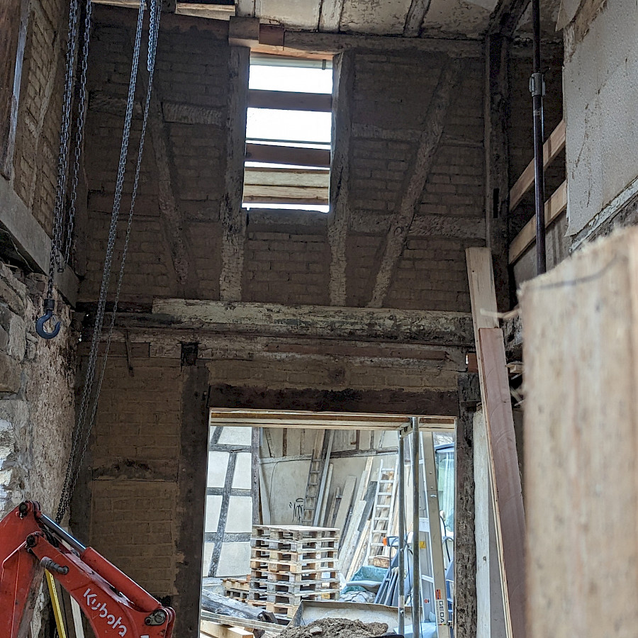 Innenansicht Eingang des Haupthauses ohne Zwischendecke, im Vordergrund ein roter Minibagger