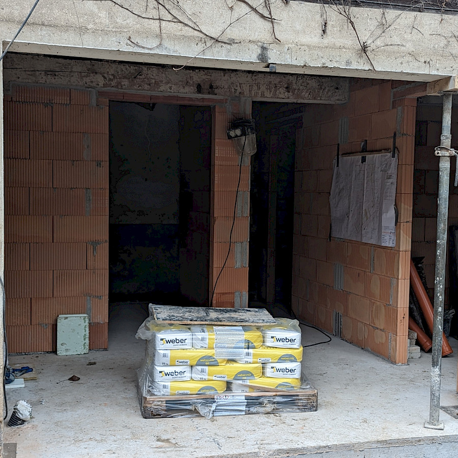 Blick ins Scheunenhaus mit neuer Bodenplatte und neu gemauerten Wänden, davor Baumaterial