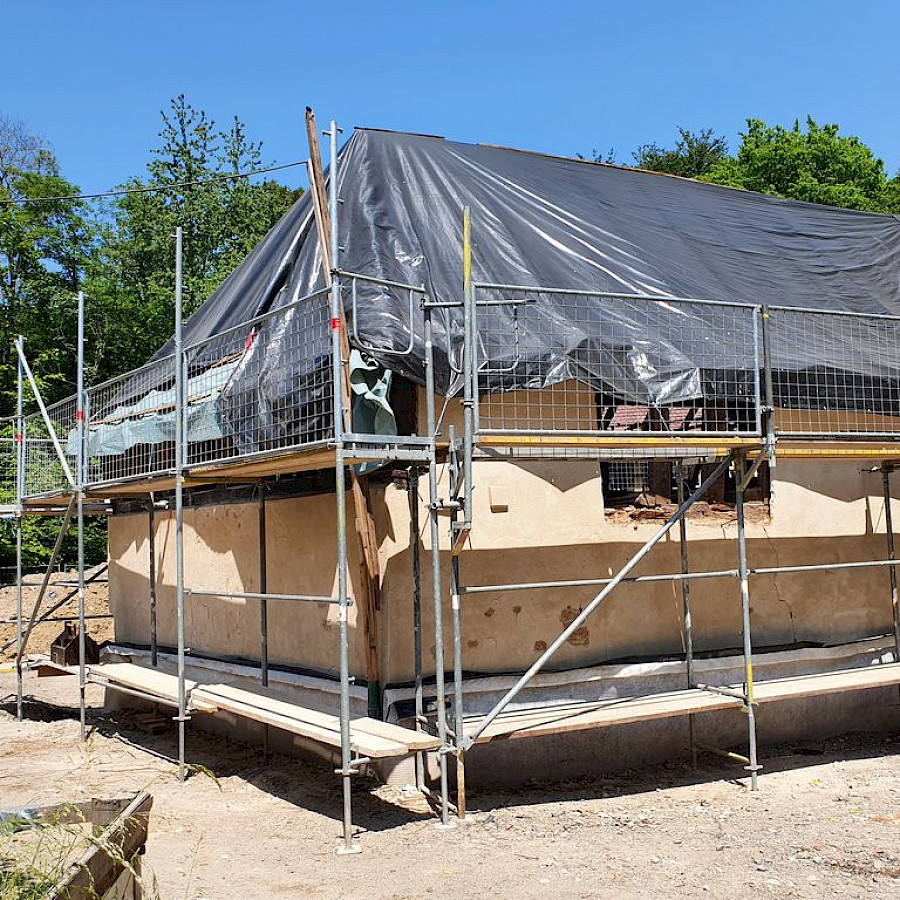 Scheunenhaus mit Gerüst und Plane über dem freigelegtem Dachstuhl, Blick von der Streuobstwiese