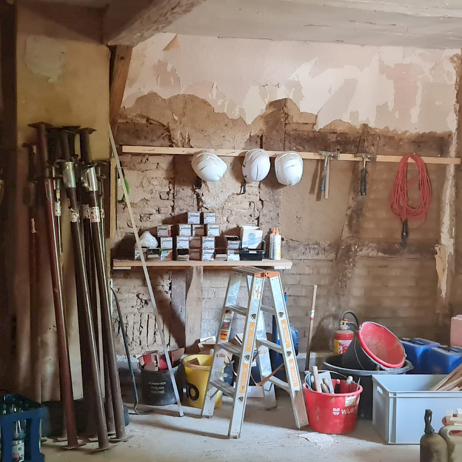 Raum des Scheunenhaus, der als Lager für diverse Arbeitsmaterialien genutzt wird, an der Wand Bauhelme