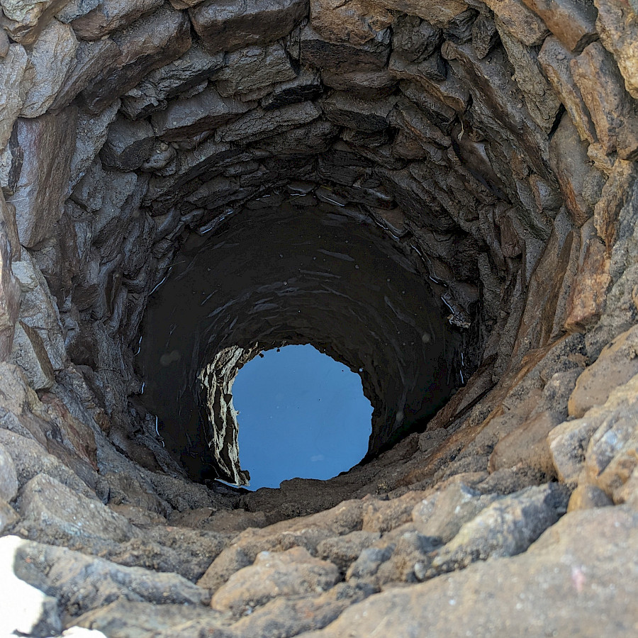 Blick in den historischen Brunnen, auf dem dessen Grund Wasser zu erkennen ist