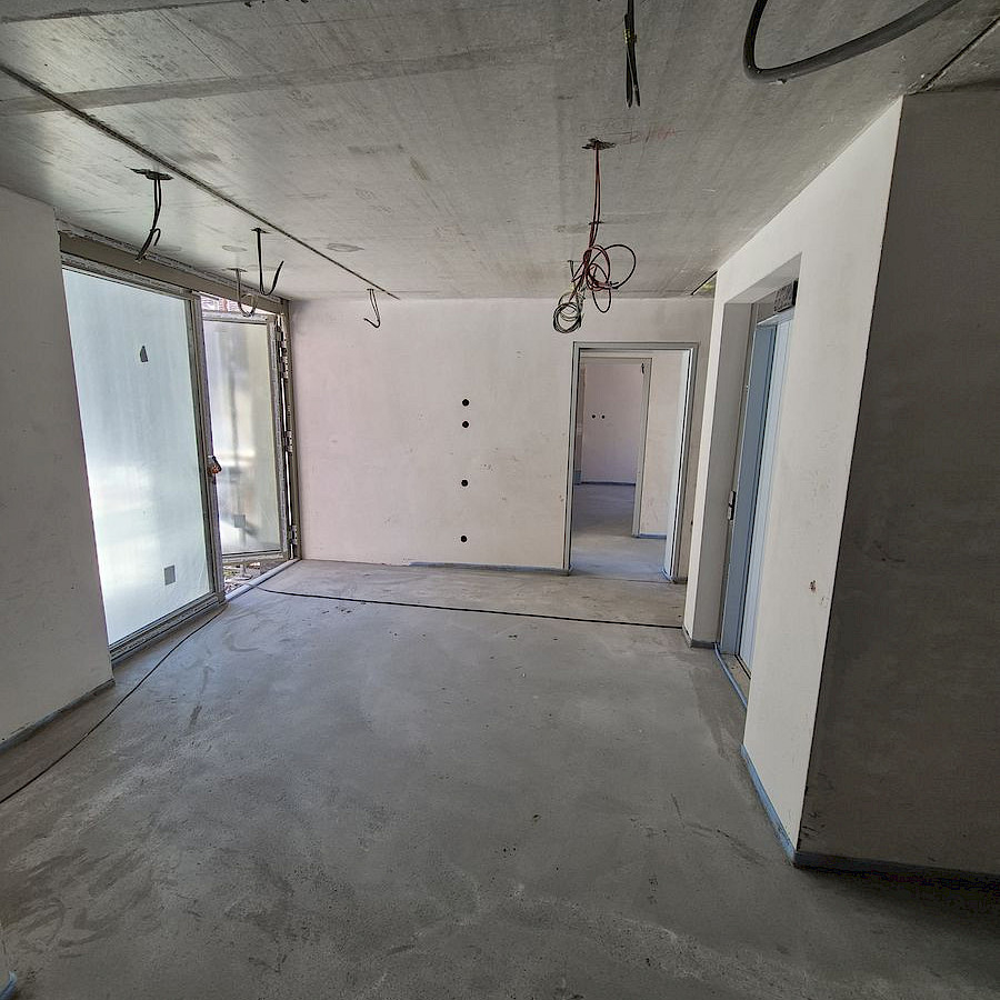 Verputzte Wände und Boden im im neuen Eckhaus, von der Decke hängen Kabel